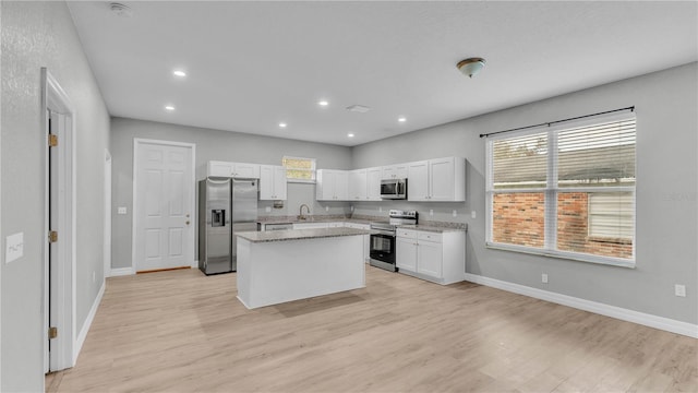 kitchen with sink, light hardwood / wood-style flooring, appliances with stainless steel finishes, white cabinets, and a kitchen island