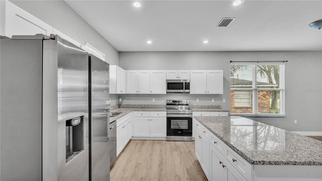 kitchen featuring appliances with stainless steel finishes, white cabinetry, a center island, light stone countertops, and light hardwood / wood-style floors