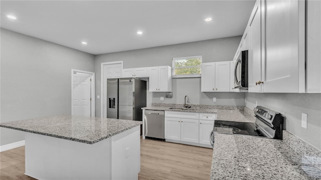 kitchen featuring sink, appliances with stainless steel finishes, white cabinetry, light stone counters, and a kitchen island