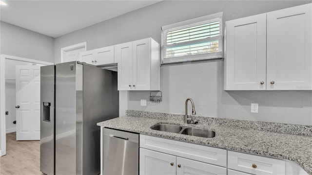 kitchen with appliances with stainless steel finishes, sink, white cabinets, light stone countertops, and light hardwood / wood-style flooring