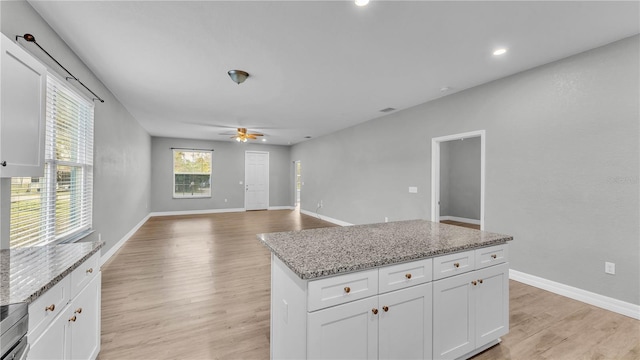 kitchen featuring ceiling fan, white cabinetry, light stone countertops, a kitchen island, and light wood-type flooring