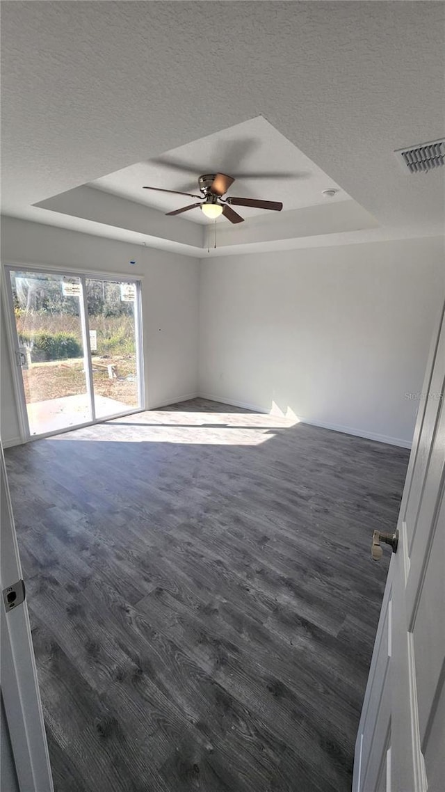 unfurnished room featuring ceiling fan, dark wood-type flooring, a textured ceiling, and a tray ceiling