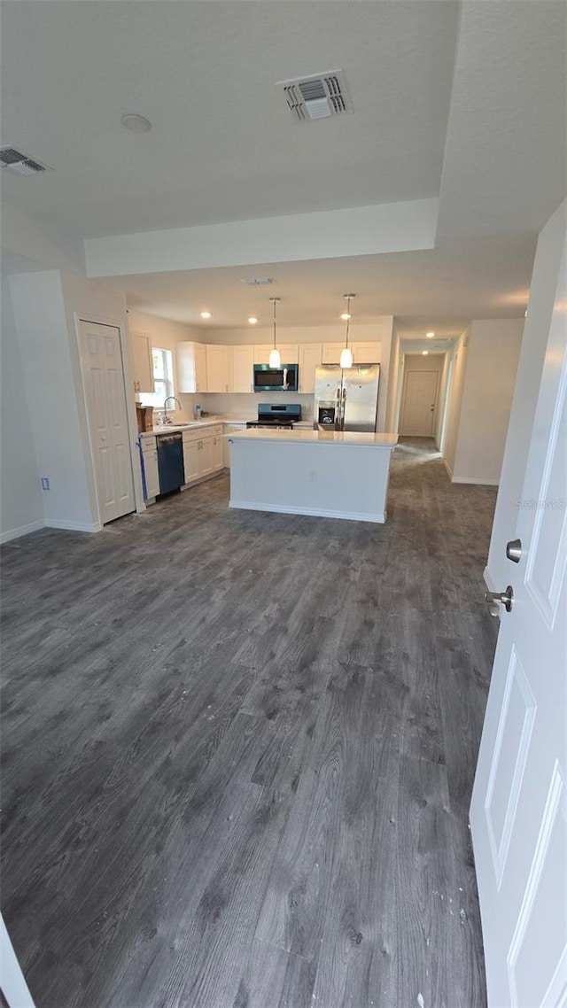 kitchen featuring pendant lighting, white cabinetry, stainless steel appliances, a center island, and dark hardwood / wood-style flooring