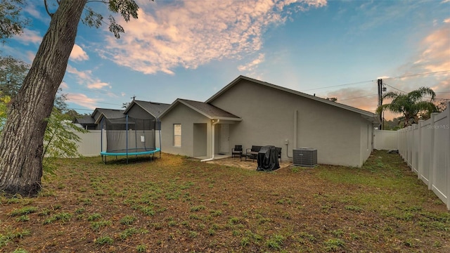 back of house with cooling unit, a fenced backyard, stucco siding, a trampoline, and a lawn