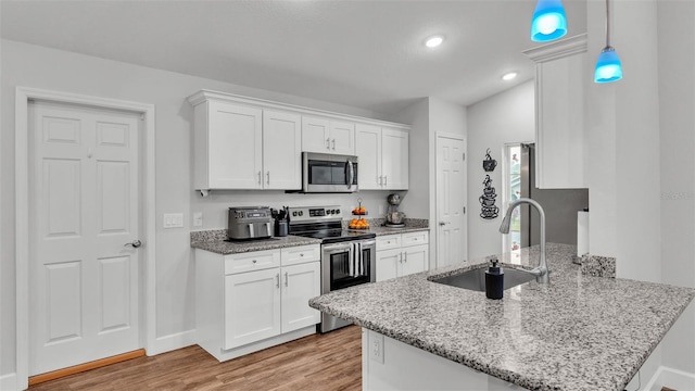 kitchen featuring a peninsula, a sink, white cabinets, light wood-style floors, and appliances with stainless steel finishes