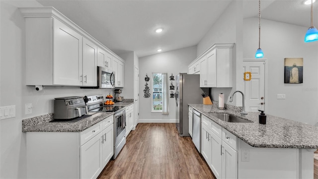 kitchen featuring a sink, a peninsula, appliances with stainless steel finishes, white cabinets, and vaulted ceiling