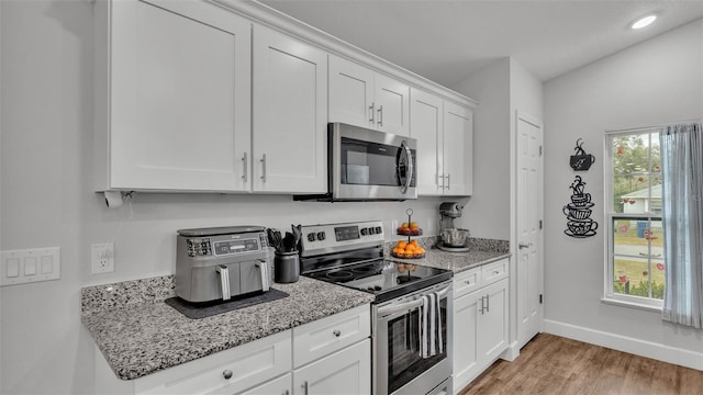 kitchen with a wealth of natural light, stainless steel appliances, light wood finished floors, and white cabinetry