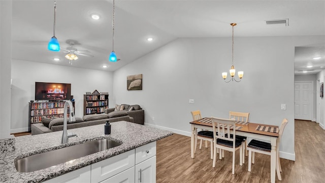 kitchen with light wood finished floors, visible vents, vaulted ceiling, ceiling fan with notable chandelier, and a sink