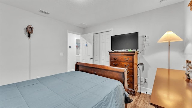 bedroom with a closet, visible vents, baseboards, and wood finished floors