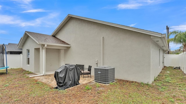 rear view of house with a trampoline, central air condition unit, stucco siding, a fenced backyard, and a patio area