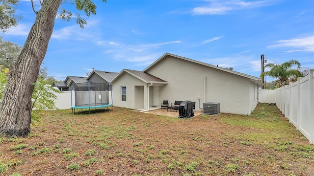 back of property featuring a trampoline, central air condition unit, stucco siding, a yard, and a fenced backyard