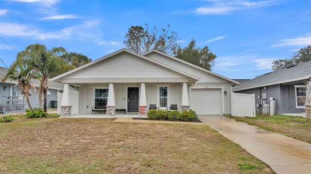 view of front facade featuring a front yard, an attached garage, covered porch, concrete driveway, and board and batten siding