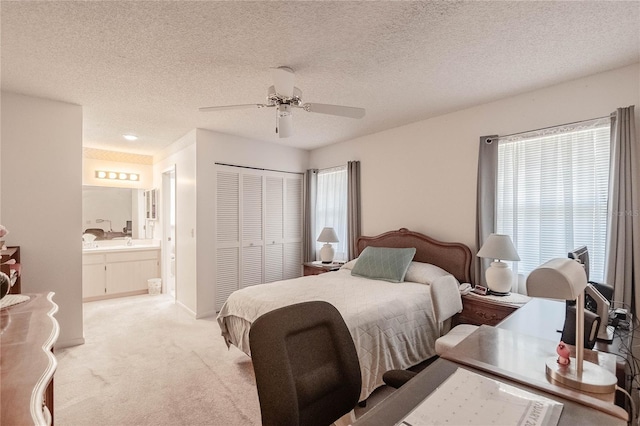 bedroom featuring ensuite bathroom, sink, light colored carpet, a textured ceiling, and a closet