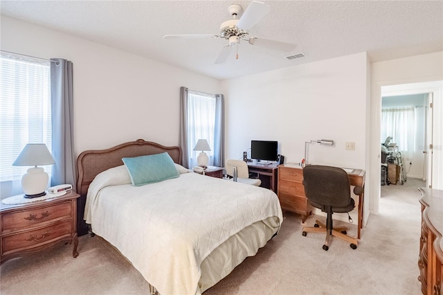 bedroom with ceiling fan, light colored carpet, and a textured ceiling