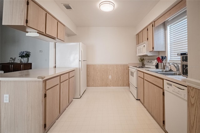 kitchen featuring light brown cabinetry, sink, white appliances, and wood walls