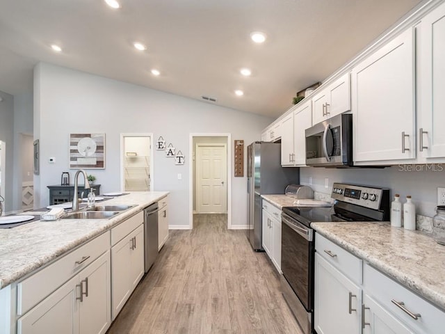 kitchen with lofted ceiling, sink, white cabinetry, stainless steel appliances, and light hardwood / wood-style floors