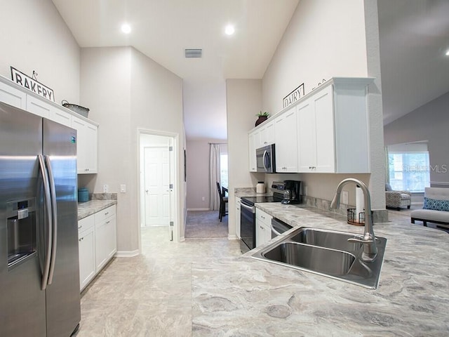 kitchen with appliances with stainless steel finishes, high vaulted ceiling, sink, white cabinets, and light stone countertops