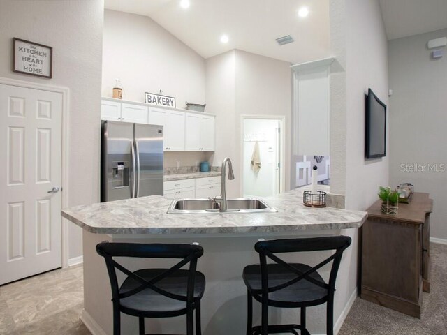 kitchen with sink, a breakfast bar, white cabinetry, stainless steel refrigerator with ice dispenser, and kitchen peninsula