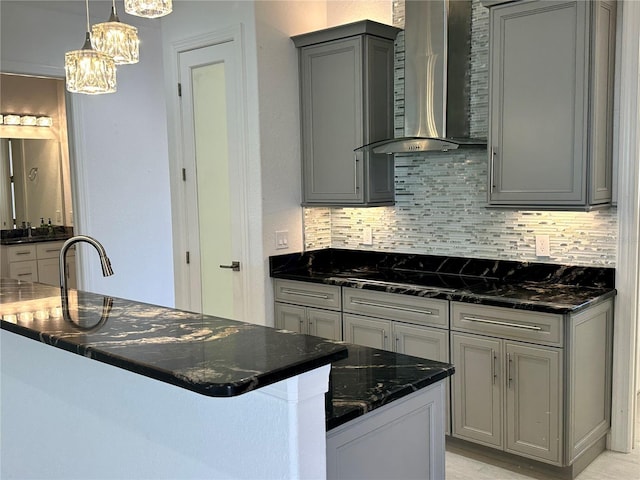 kitchen featuring gray cabinets, backsplash, dark stone counters, hanging light fixtures, and wall chimney exhaust hood