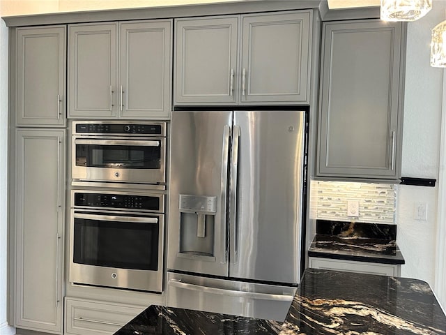 kitchen featuring decorative backsplash, gray cabinets, stainless steel appliances, and dark stone counters