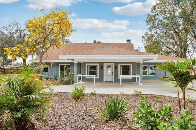 ranch-style home featuring roof with shingles, a chimney, a porch, and stucco siding