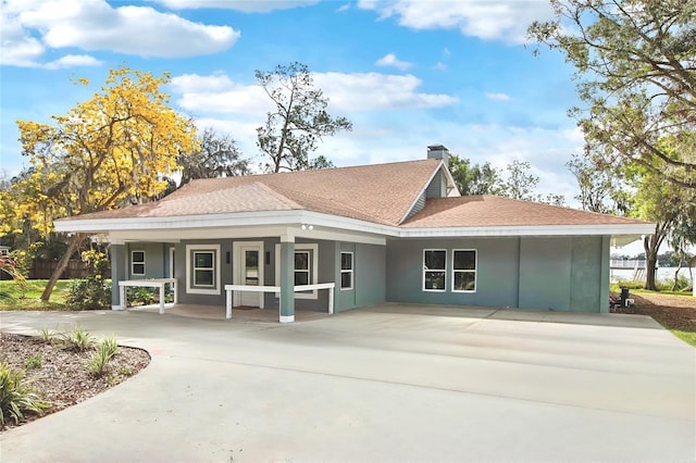 rear view of house featuring driveway, a shingled roof, and stucco siding