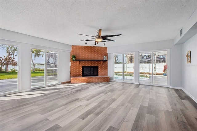 unfurnished living room featuring a textured ceiling, wood finished floors, a ceiling fan, baseboards, and a brick fireplace