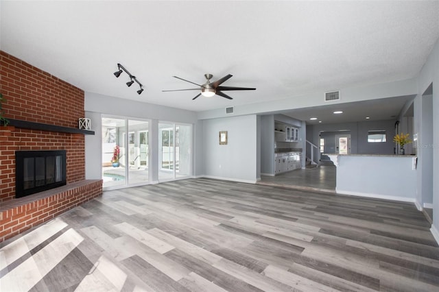 unfurnished living room with a brick fireplace, wood finished floors, visible vents, and baseboards