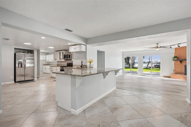 kitchen featuring visible vents, a peninsula, stainless steel appliances, stone counters, and a sink