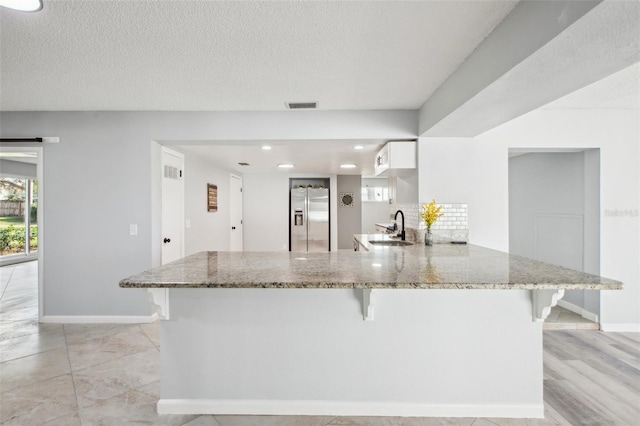 kitchen with a barn door, a sink, light stone countertops, a peninsula, and stainless steel fridge with ice dispenser