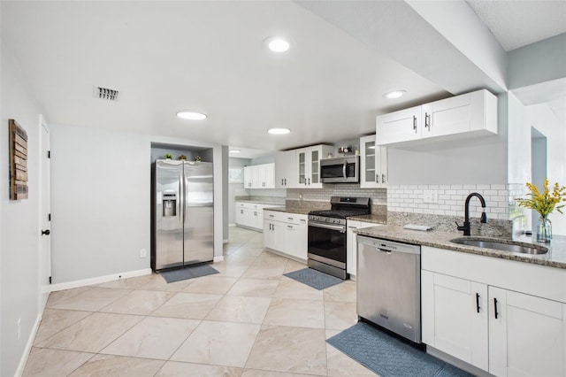 kitchen with stainless steel appliances, tasteful backsplash, visible vents, a sink, and light stone countertops