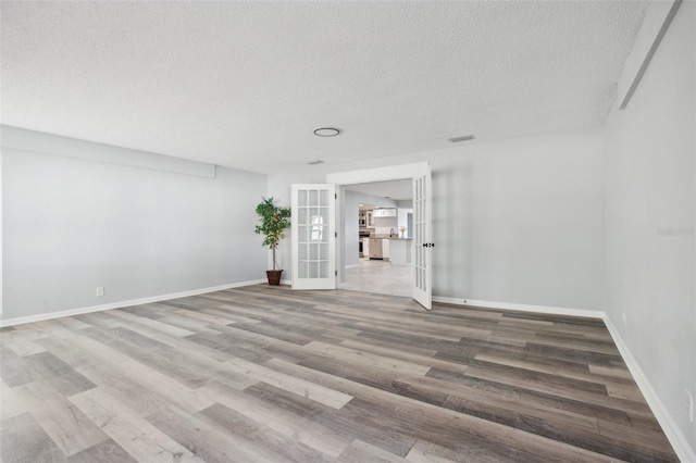 spare room featuring baseboards, visible vents, wood finished floors, a textured ceiling, and french doors