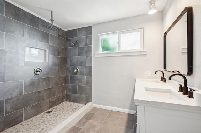 full bath with a tile shower, double vanity, a sink, and baseboards