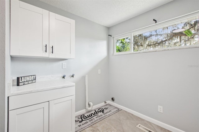 clothes washing area featuring a textured ceiling, light tile patterned floors, washer hookup, baseboards, and cabinet space