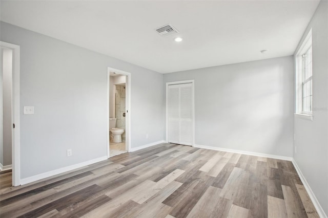 unfurnished bedroom with connected bathroom, wood finished floors, visible vents, baseboards, and a closet