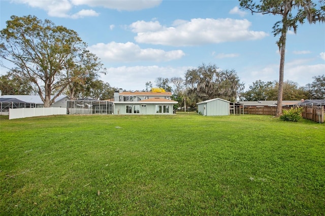 view of yard featuring a lanai, a fenced backyard, a storage unit, and an outbuilding