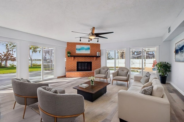 living room featuring baseboards, ceiling fan, wood finished floors, a textured ceiling, and a fireplace