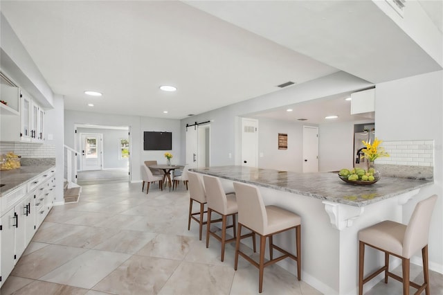 kitchen featuring a barn door, a peninsula, visible vents, white cabinetry, and a kitchen bar