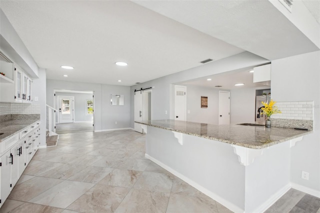 kitchen with visible vents, a barn door, a breakfast bar, and white cabinets