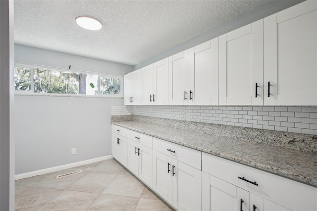 kitchen featuring baseboards, tasteful backsplash, light stone countertops, and white cabinets