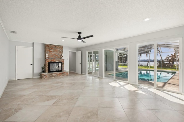 unfurnished living room with ceiling fan, a textured ceiling, light tile patterned flooring, visible vents, and a brick fireplace