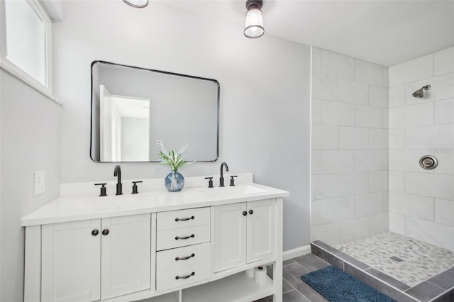 bathroom with a tile shower, double vanity, and a sink