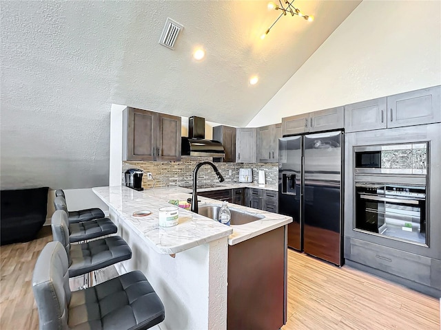 kitchen featuring sink, appliances with stainless steel finishes, a kitchen breakfast bar, kitchen peninsula, and wall chimney range hood