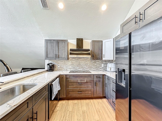 kitchen featuring lofted ceiling, wall chimney exhaust hood, tasteful backsplash, kitchen peninsula, and stainless steel appliances