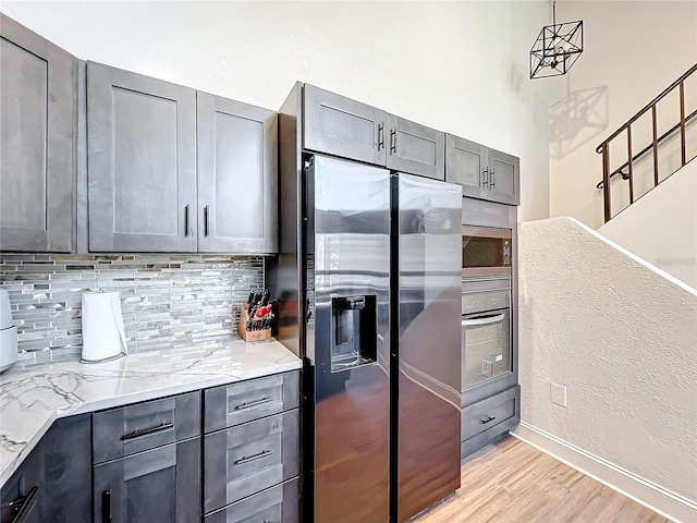 kitchen with decorative light fixtures, decorative backsplash, light stone counters, stainless steel appliances, and light hardwood / wood-style flooring