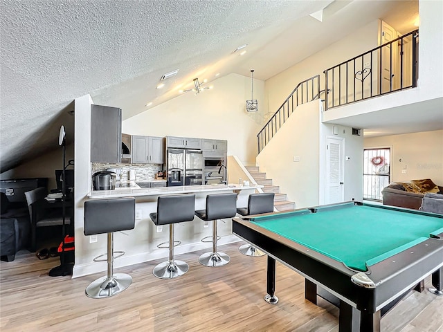 playroom featuring light hardwood / wood-style flooring, vaulted ceiling, billiards, and a textured ceiling