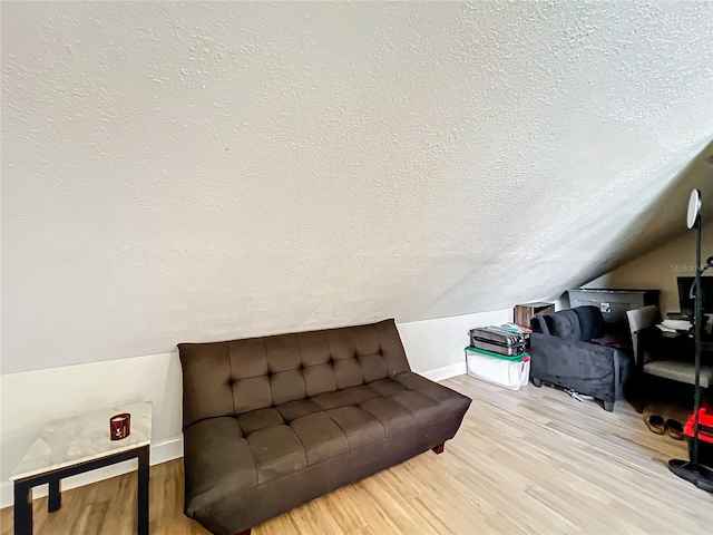 sitting room with vaulted ceiling, light wood-type flooring, and a textured ceiling