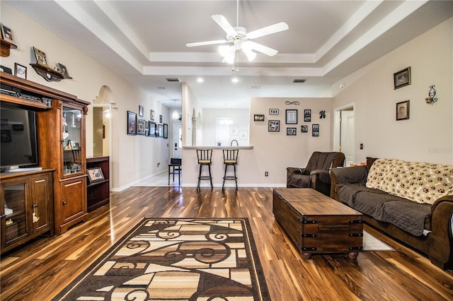 living room with a raised ceiling, ceiling fan, and dark hardwood / wood-style flooring