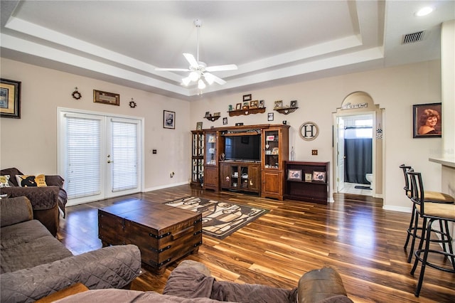 living room featuring dark hardwood / wood-style flooring, a tray ceiling, and a healthy amount of sunlight