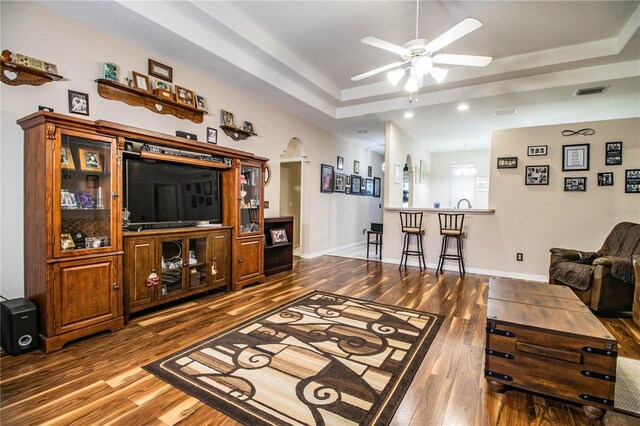 living room featuring ceiling fan, dark hardwood / wood-style flooring, and a tray ceiling